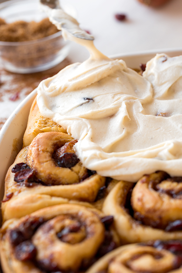 Orange Cinnamon Rolls Being Spread with Rich Frosting | thecozyapron.com