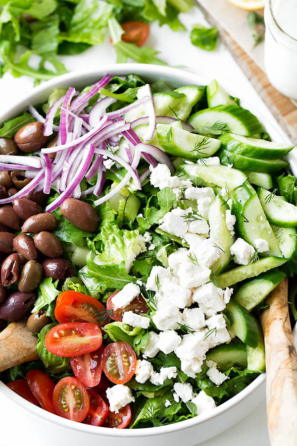 Greek Salad ingredients in a large bowl, with a wooden spoon | thecozyapron.com