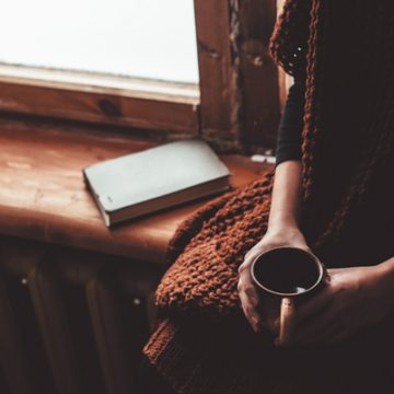 Woman sitting in silence with a cup of coffee and a book