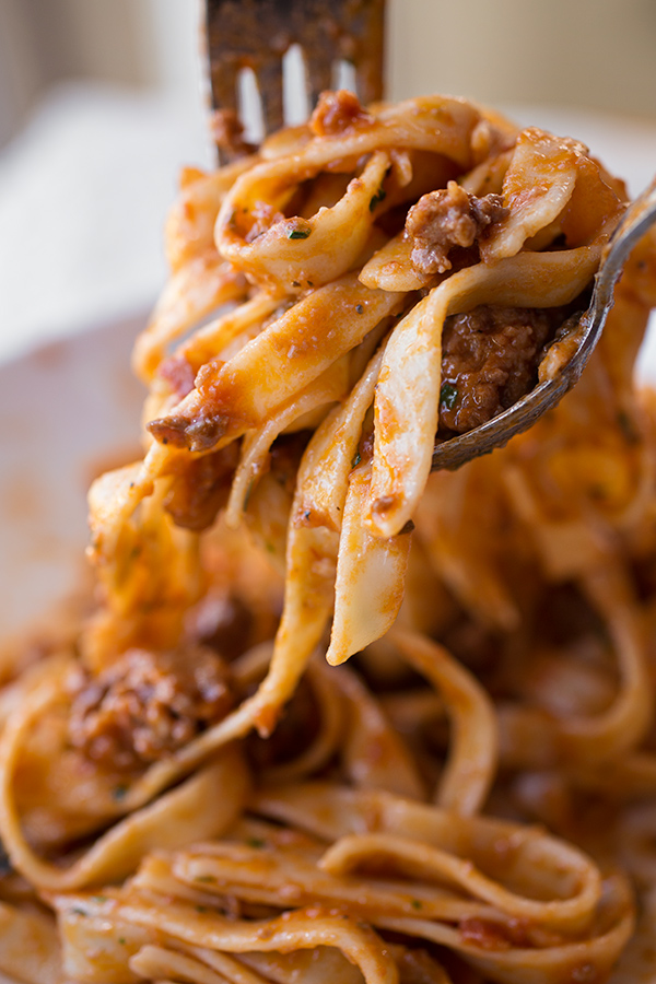 Fork in spoon filled with Fettuccine Bolognese with Sausage | thecozyapron.com